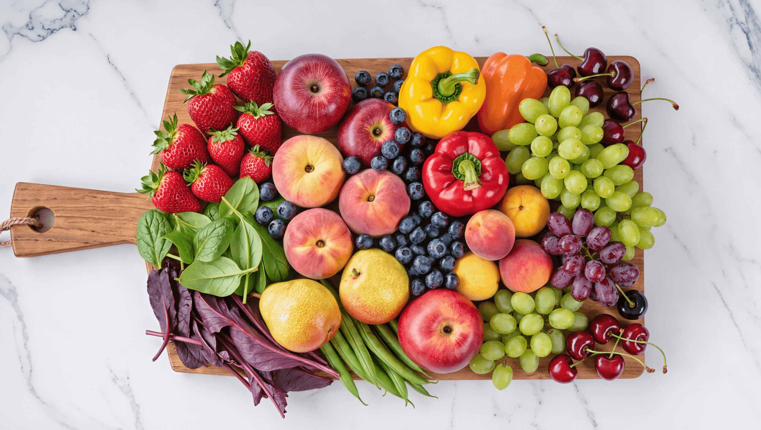 Fresh Dirty Dozen produce including strawberries, spinach, kale, peaches, apples, grapes, and bell peppers arranged on a wooden cutting board