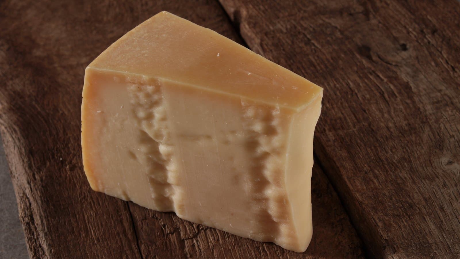 A wedge of aged cheese on a dark wooden board