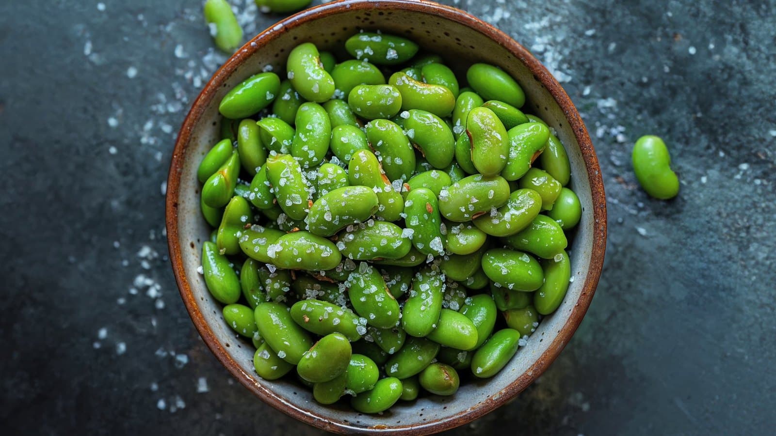 A bowl of shelled green edamame beans with sea salt on a dark table