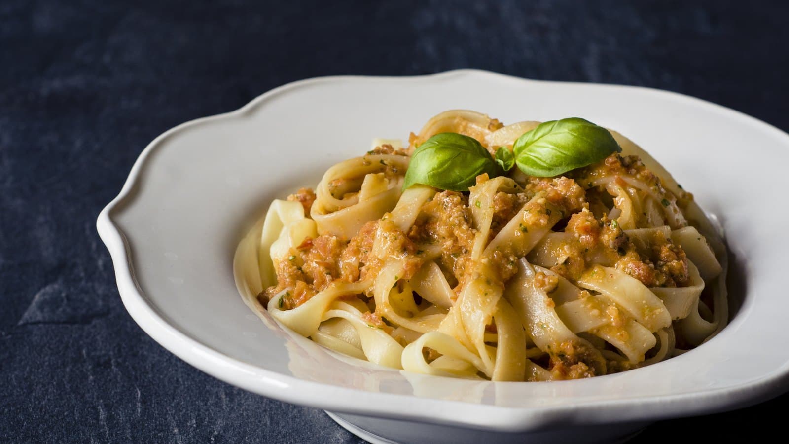 A white bowl of fettuccine pasta with sauce and fresh basil