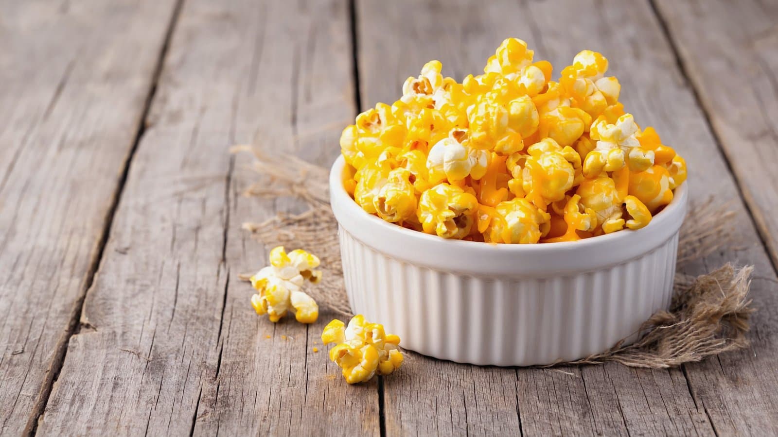 A white bowl of cheese popcorn on a wooden table